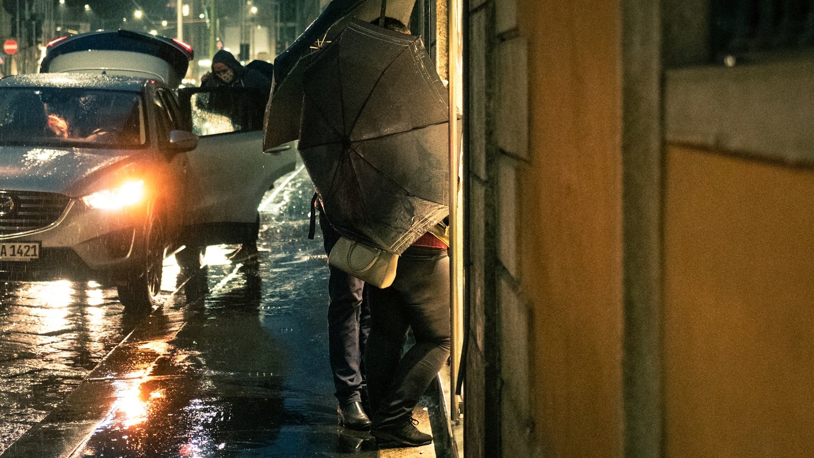man in black jacket and blue denim jeans holding umbrella walking on sidewalk during daytime