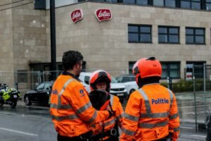 Police officers in orange jackets stand outside lotus building.
