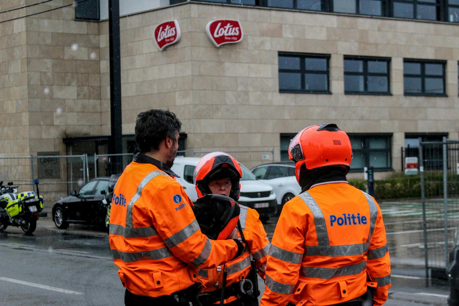 Police officers in orange jackets stand outside lotus building.